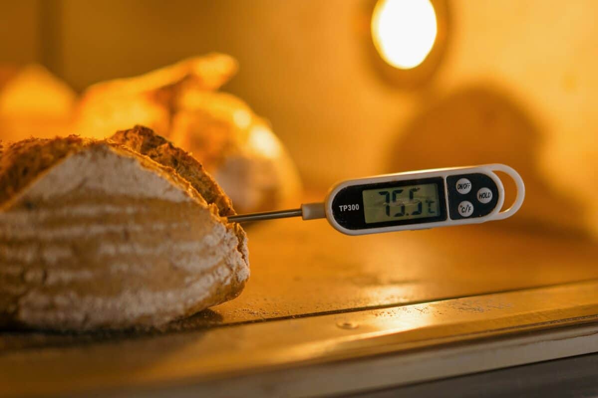 baker measures the temperature of freshly baked bread in the oven with a thermometer