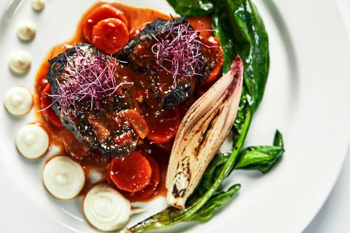 Braised beef cheeks with vegetables on a white plate Cooking beef cheeks in demigas sauce with