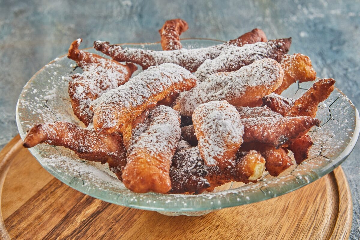 Bugnes, beignets français dans une assiette transparente sur une planche en bois