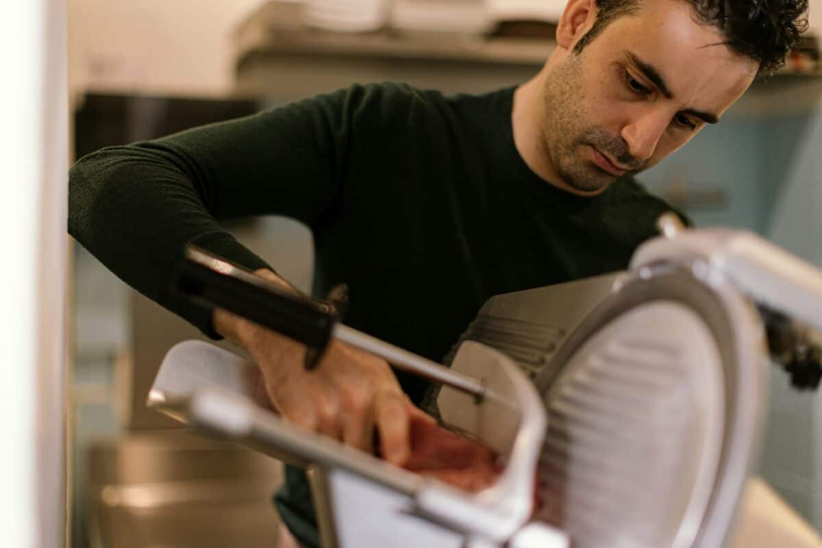 butcher slices ham using electric slicer