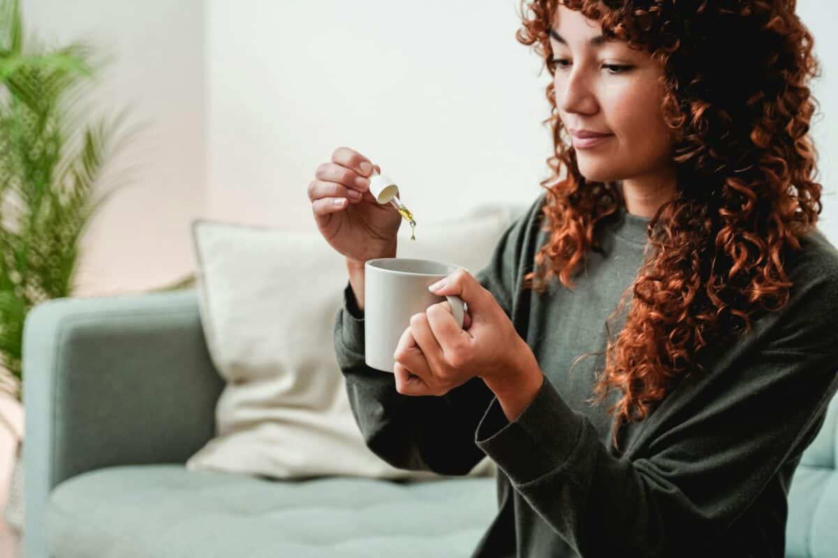Goutte à goutte d'huile de CBD - Jeune femme prenant de l'huile de cannabis dans une boisson au thé pour traiter l'anxiété et le stress