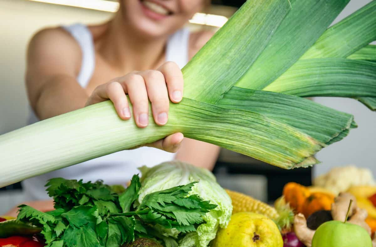 Cheerful young woman in the kitchen holds a leek in her hands.