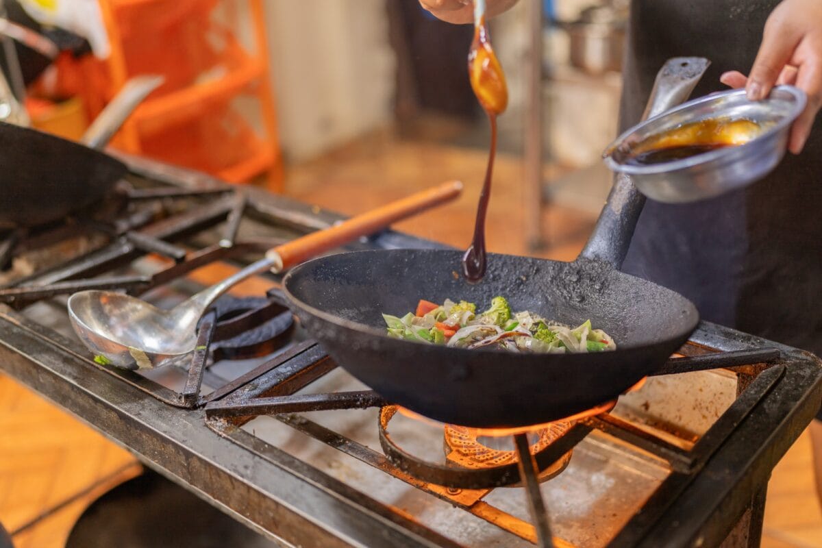 Chef adding sauce to mixed vegetables in a frying pan