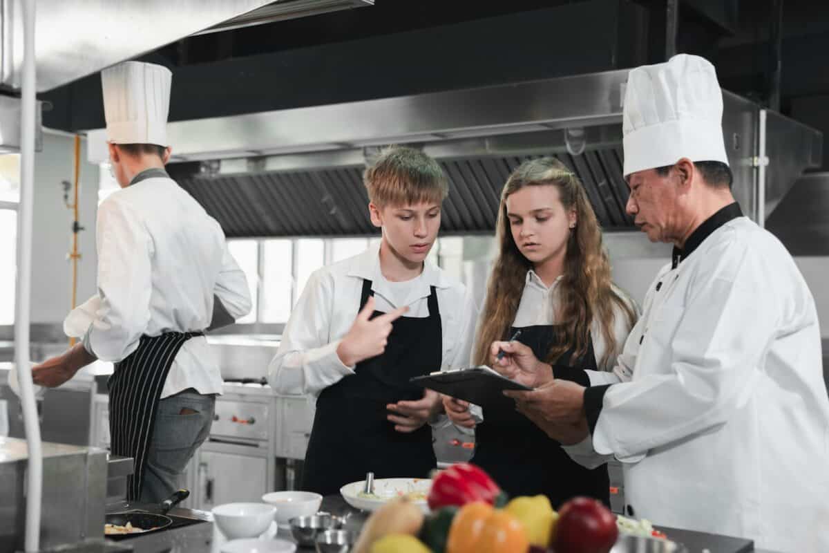 Chef and students cooking and preparing food in kitchen. Cooking class for children.