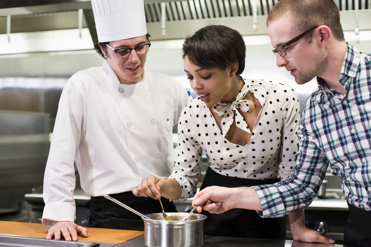 Chef masculin donnant un cours de cuisine à deux élèves.