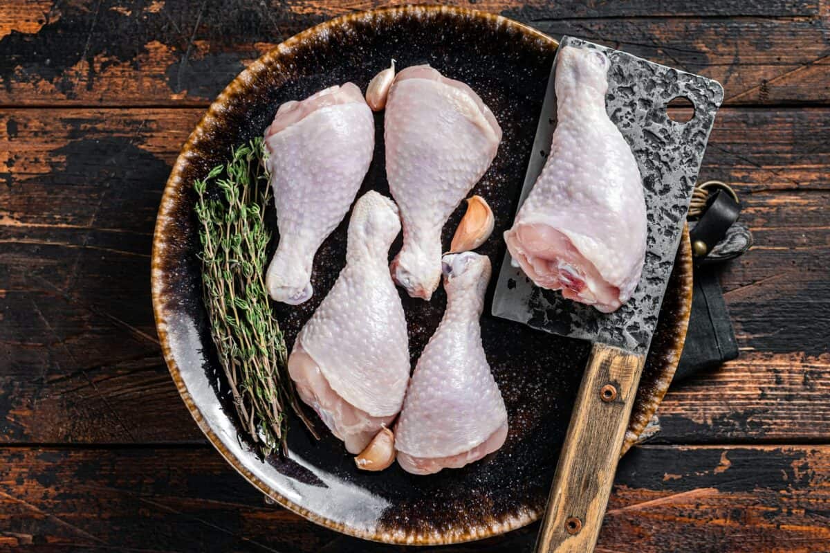Chicken drumsticks legs, raw poultry meat on butcher board. Wooden background. Top view