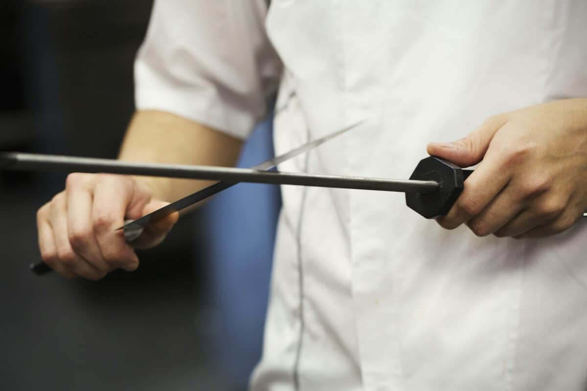 Close up of a chef sharpening a knife with a honing steel.