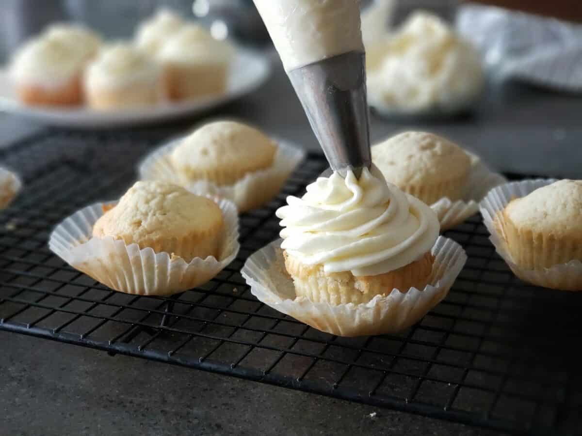 Close up of a pastry bag piping white icing on cupcakes