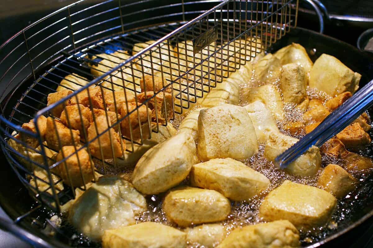 Close-up of golden brown stinky tofu frying in hot oil in a deep fryer.