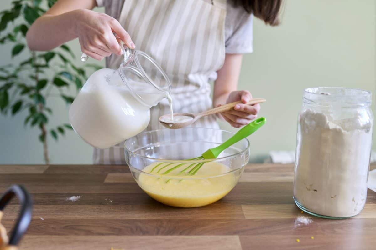 Close-up process of preparing orange pancakes, female hands pouring milk into bowl