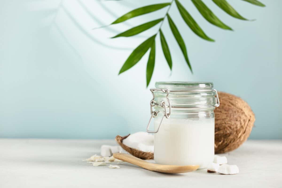 Coconut oil in jar with fresh coconut and tropical leaf shadow, Spa cosmetic and food ingredient
