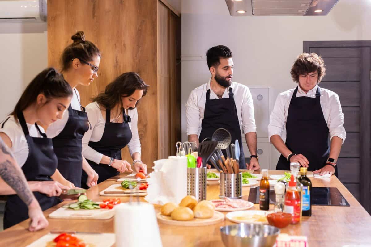Cooking course - senior male chef in cook uniform teaches young people cooking class students to