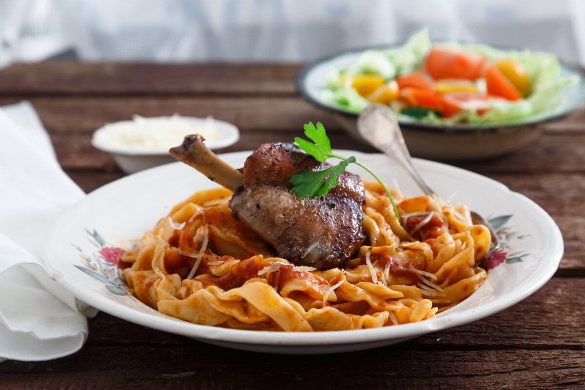 Cuisse de lapin braisée dans une sauce tomate avec des pâtes maison, fond rustique sombre