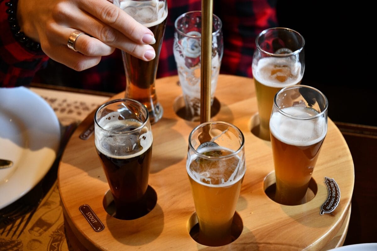 Dégustation de bière sur un plateau en bois. Une main féminine prend un verre de bière artisanale
