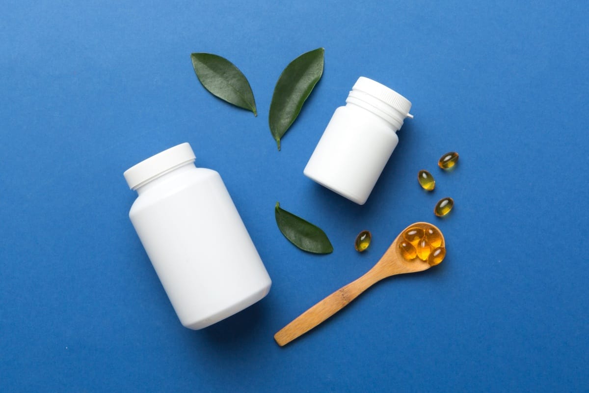 Omega-3 capsules lie in white bottle on a table with green leaves