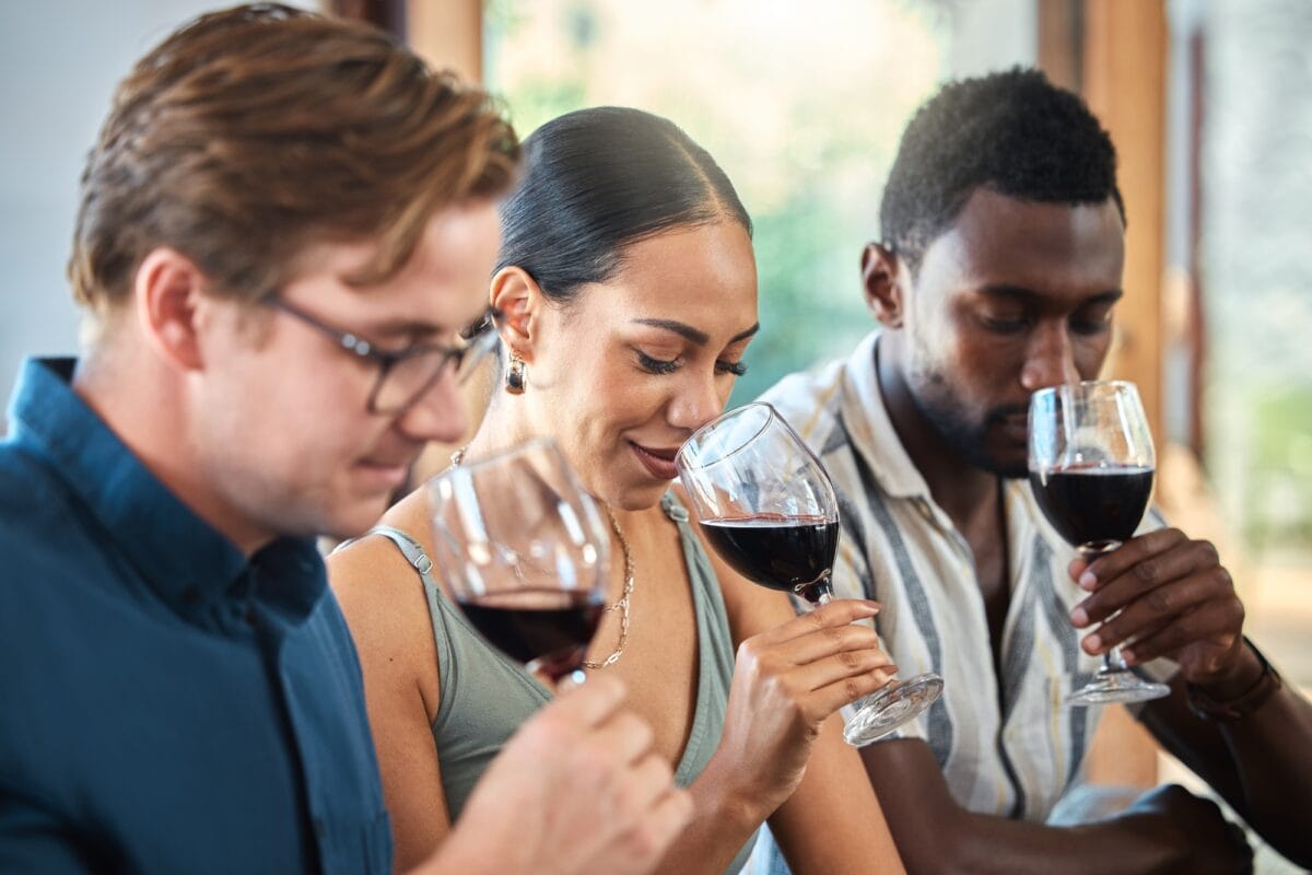 Diversity, luxury and friends wine tasting at a restaurant or vineyard, smelling alcohol in a glass