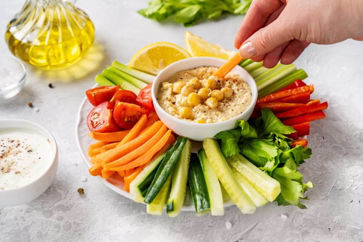 Female hand dipping carrot stick into hummus