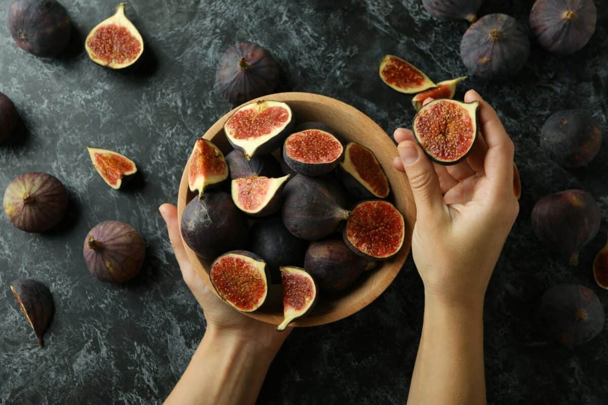 Female hands hold bowl with fig on black smokey background