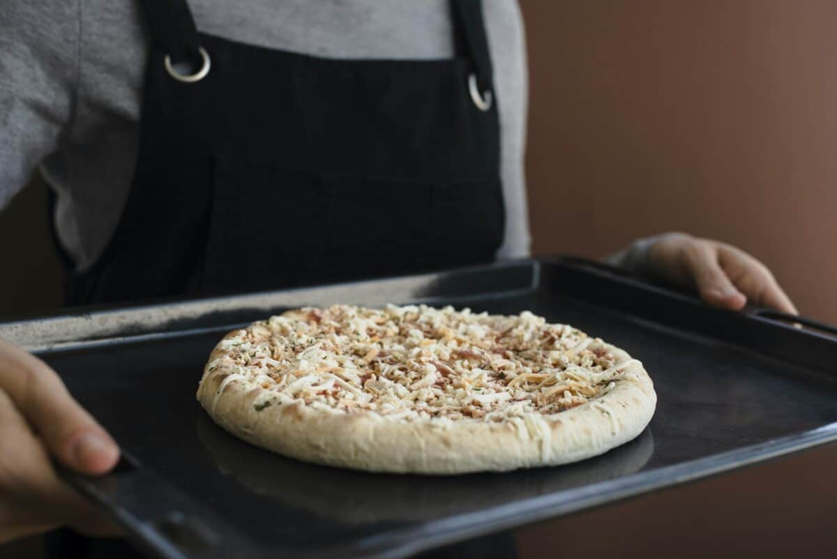 Femme tenant une plaque de four avec une pizza surgelée