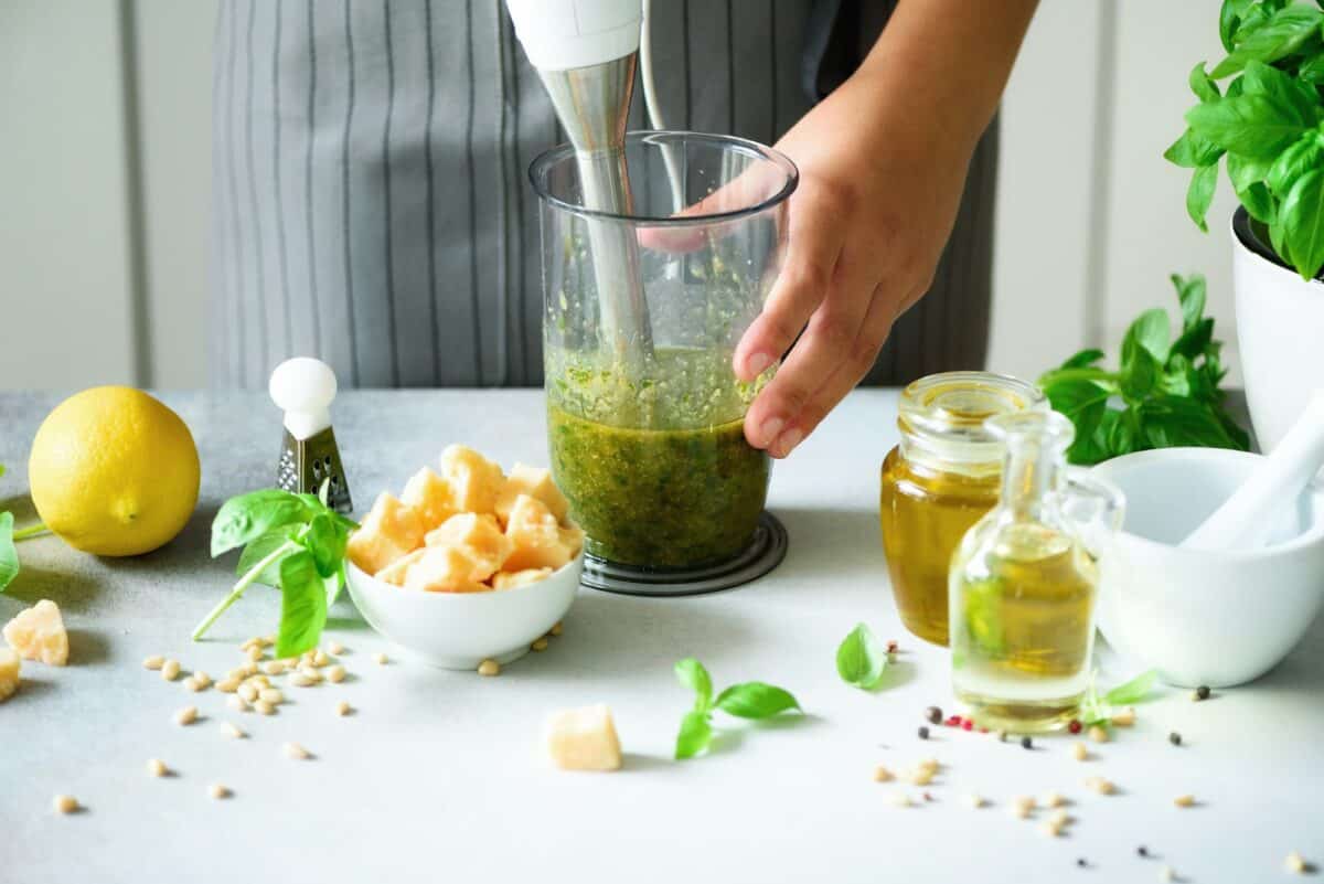 Femme utilisant un mixeur à main pour faire du pesto. Cuisine blanche design intérieur. Espace de copie. Végétarien, propre