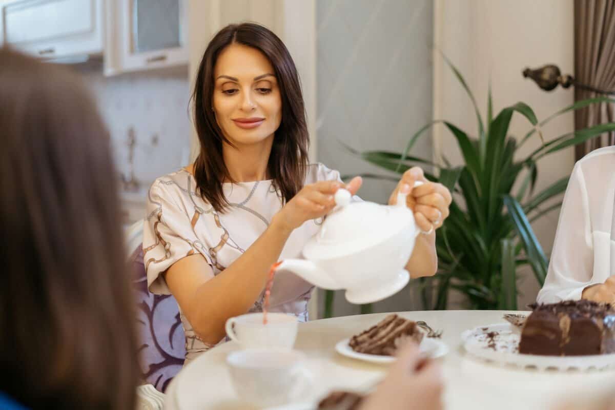 Femme versant du thé dans une théière blanche à la maison