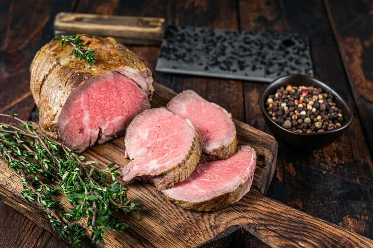 Filet de bœuf rôti sur une planche en bois avec des herbes. Fond en bois foncé. Vue de dessus