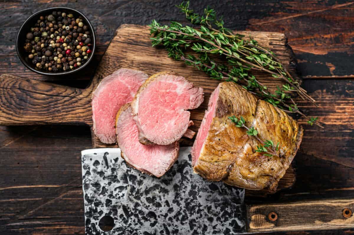 Filet de bœuf rôti sur une planche en bois avec des herbes. Fond en bois foncé. Vue de dessus