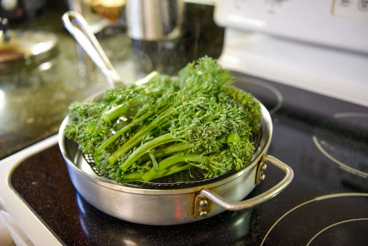 Fresh broccolini sits in a steamer basket waiting to be steamed.
