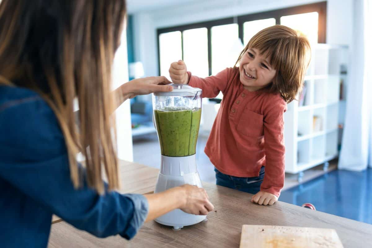 Garçon aidant sa mère à préparer un jus de désintoxication avec un mixeur dans la cuisine à la maison.