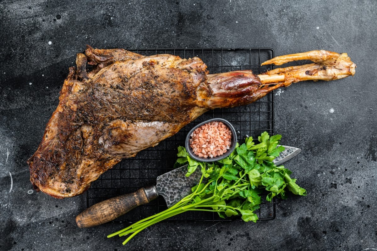 BBQ Roasted lamb mutton leg with herbs and spices on a grill. Black background. Top view