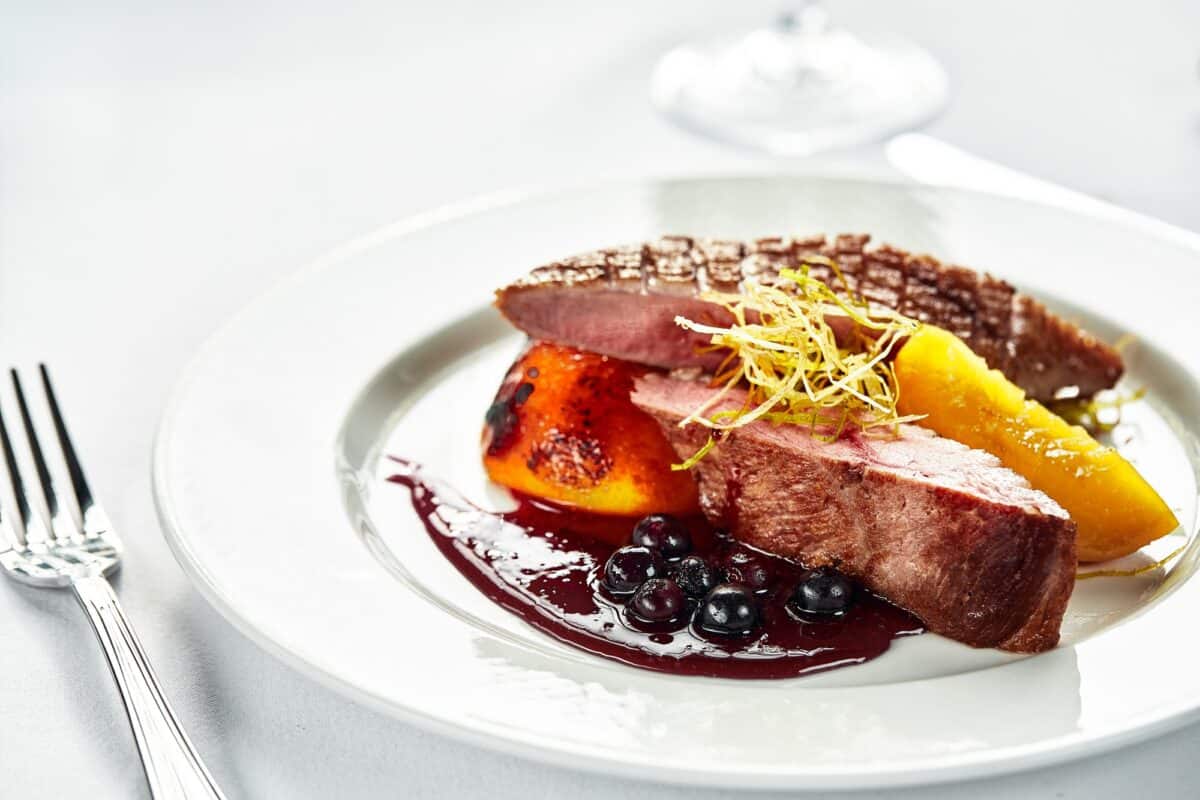 Grilled duck breast with peaches in berry sauce, grilled duck fillet on a white plate, close-up of