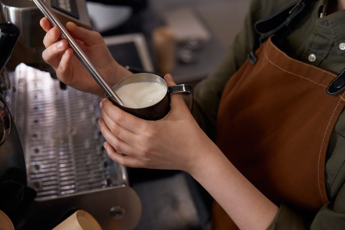 Gros plan d'un barista préparant un café au lait avec de la mousse de lait sur une machine à café.