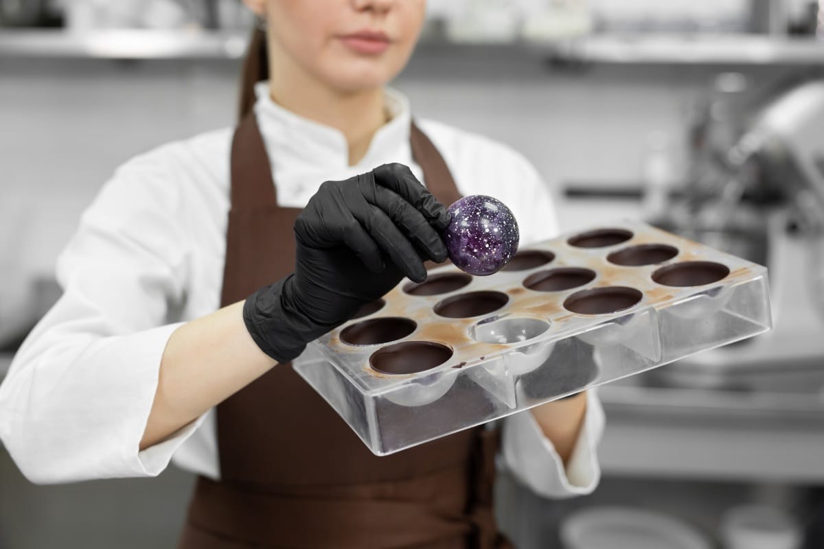 Gros plan sur une pâtissière qui démoule un bonbon au chocolat fait à la main dans un moule en polycarbonate.