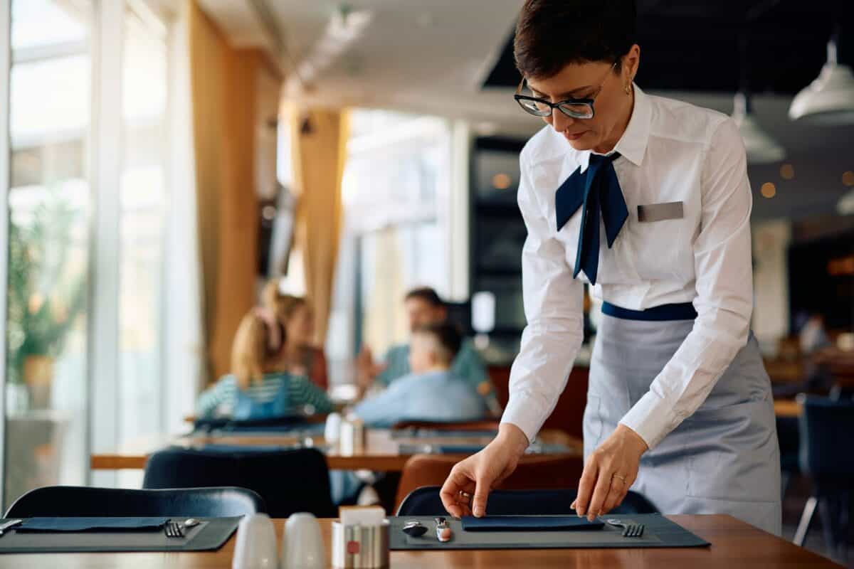 Hotel waitress setting dining tables in a restaurant.