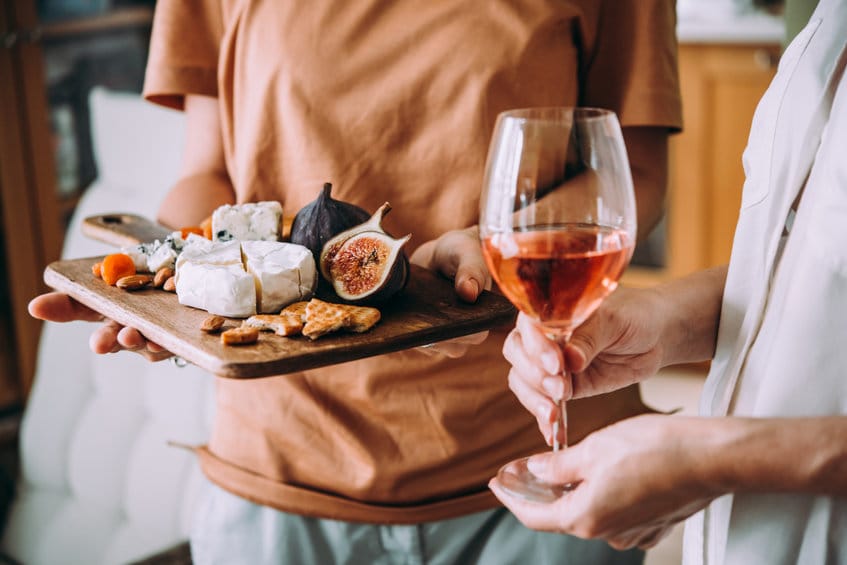 Mains tenant un verre de vin et une planche en bois contenant différentes sortes de fromages et de fruits secs. Concept de dîner ou d'apéritif.
