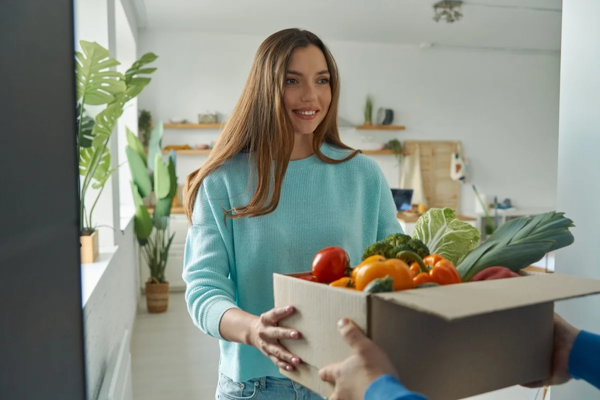 Jeune femme heureuse acceptant une boîte contenant des provisions de la part d'un livreur à domicile