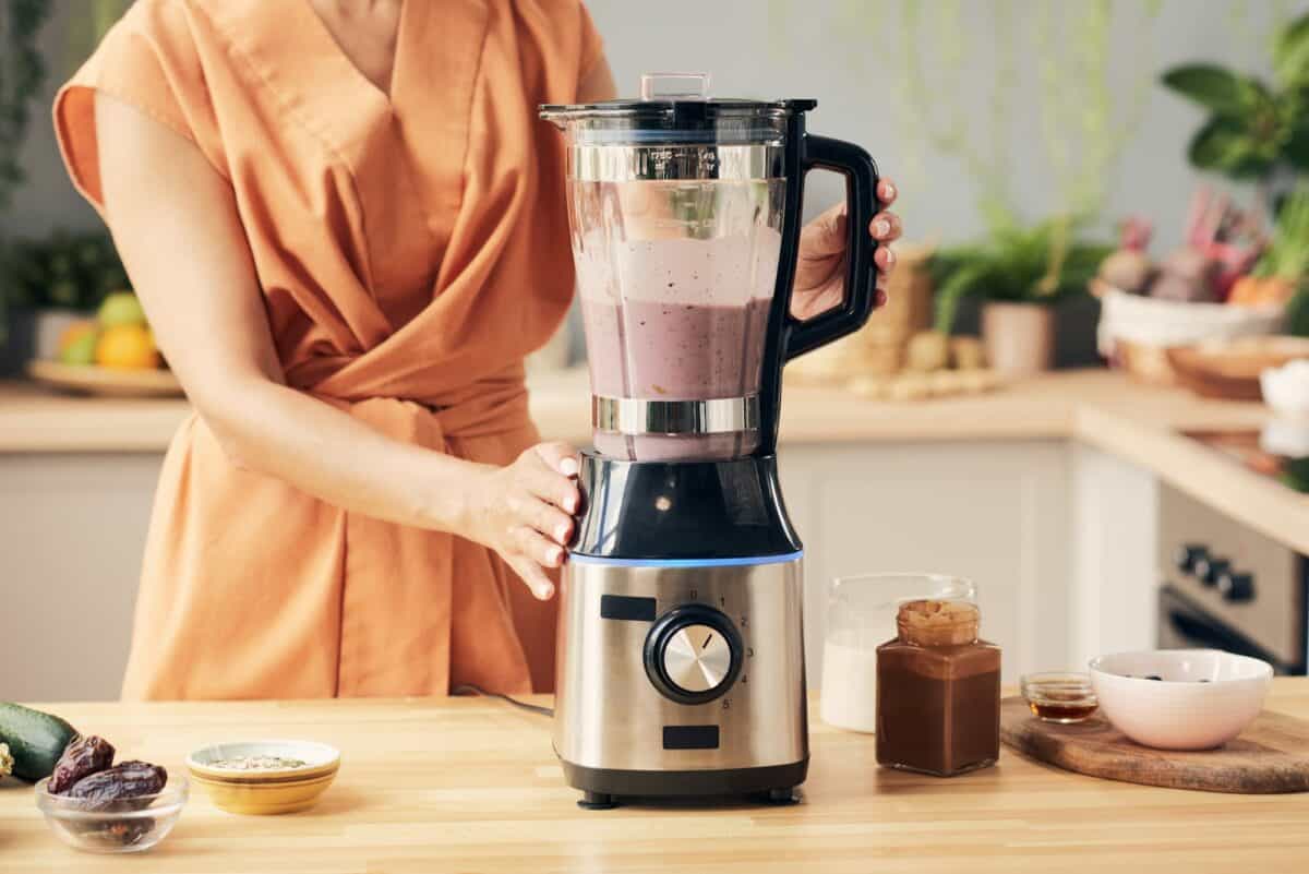 Main d'une jeune femme préparant un smoothie dans un mixeur