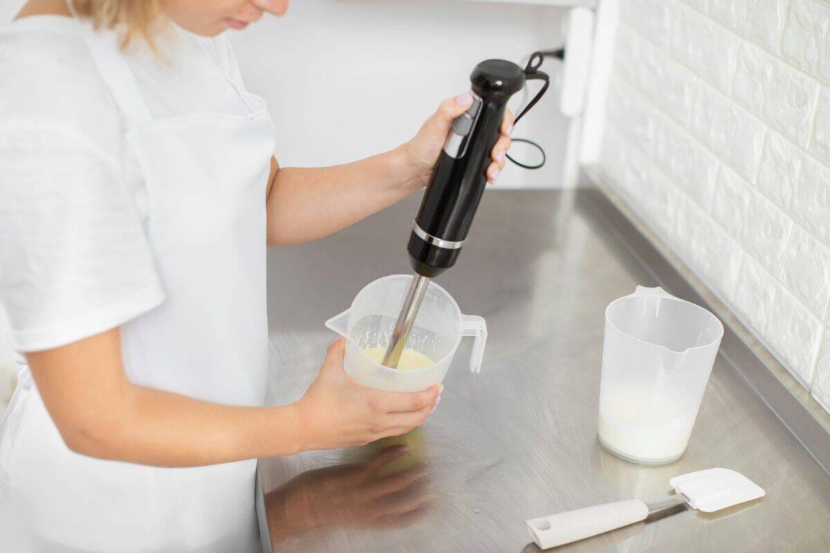 Mains d'une pâtissière professionnelle tenant le mixeur à main