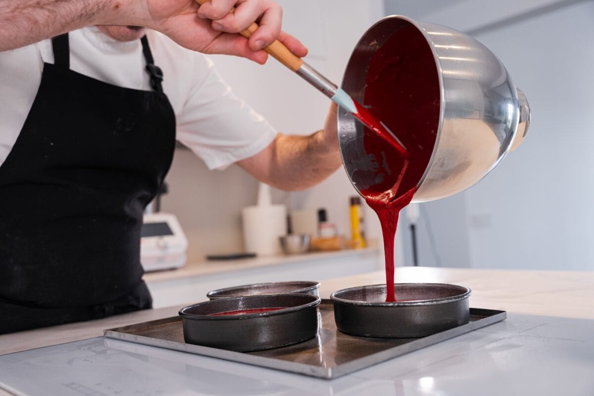 man cooking a red velvet cake at home, adding the sponge cake in the molds before putting