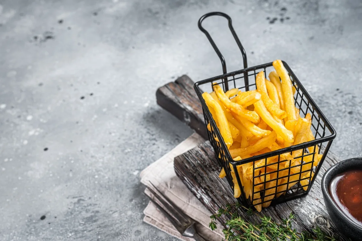 Panier de pommes de terre frites avec du sel sur une planche en bois. Fond gris.