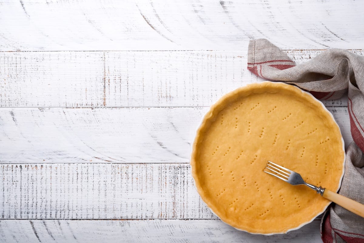Pâte à quiche, tarte ou tarte au four dans un moule en céramique, prête à cuire sur un torchon de cuisine.