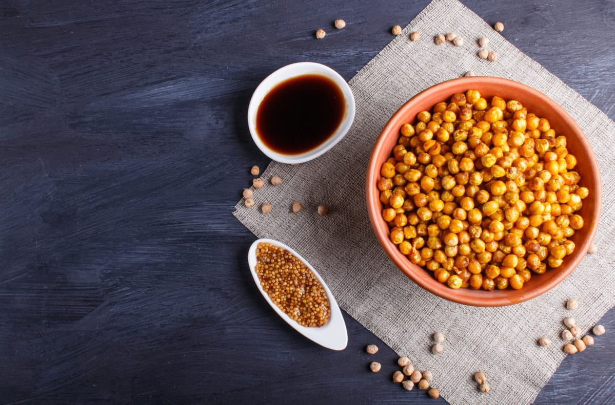 Pois chiches frits avec épices dans une assiette en terre cuite sur fond noir en bois.