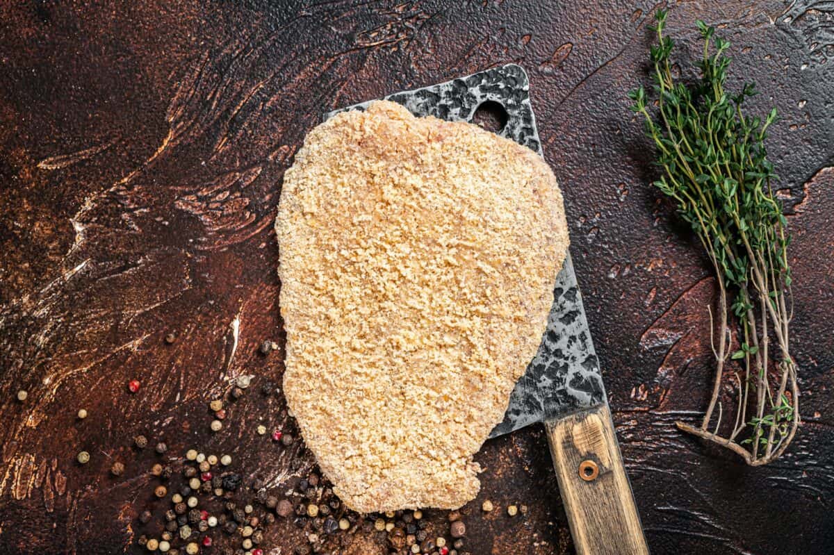 Pork Raw Escalope or schnitzel on a meat cleaver with herbs. Dark background. Top view