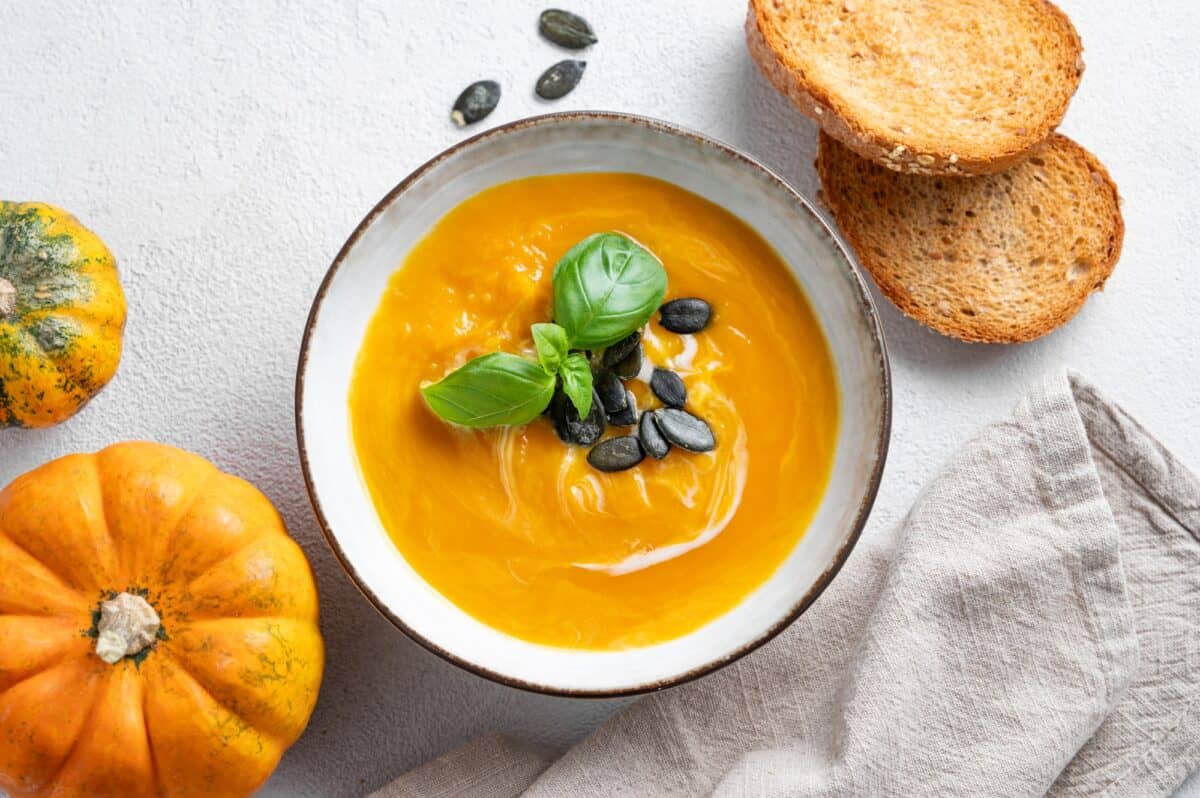 Pumpkin soup with cream, basil and seeds on a light background with bread, fresh pumpkins