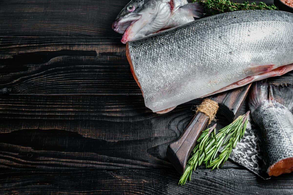 Raw cut salmon fish on a wooden cutting board with chef cleaver. Black