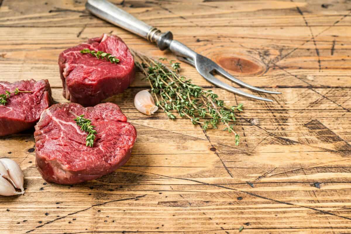 Raw Fillet mignon steaks, beef tenderloin on a wooden butcher table with meat fork.