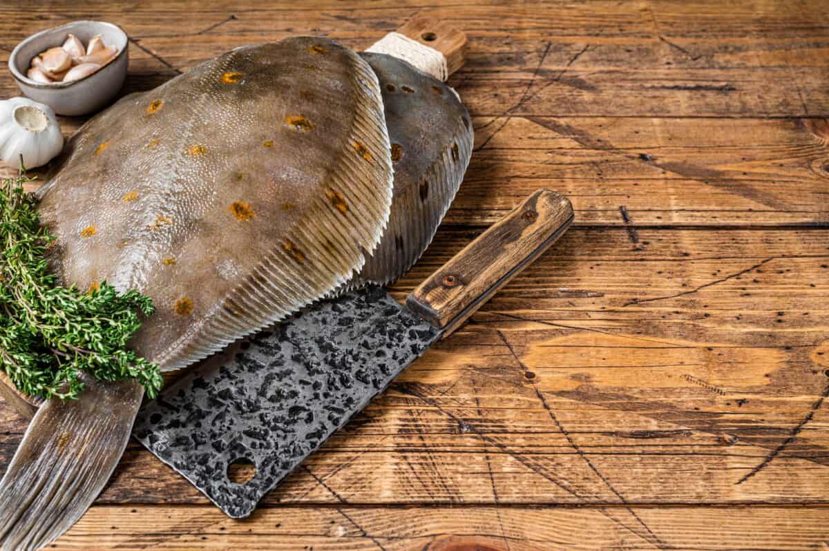 Raw flounder flatfish on butcher board with cleaver. wooden background. Top view. Copy space