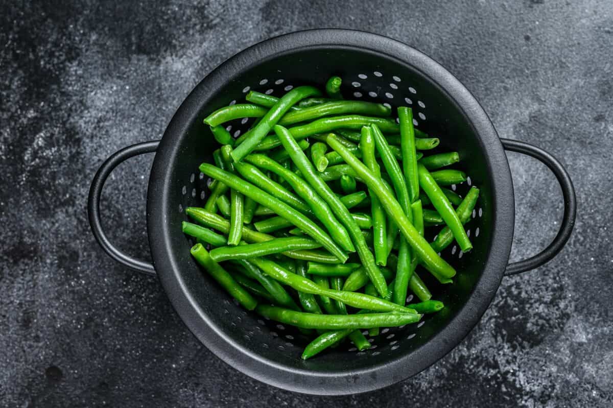 Raw green beans in a colander. Black background. top view