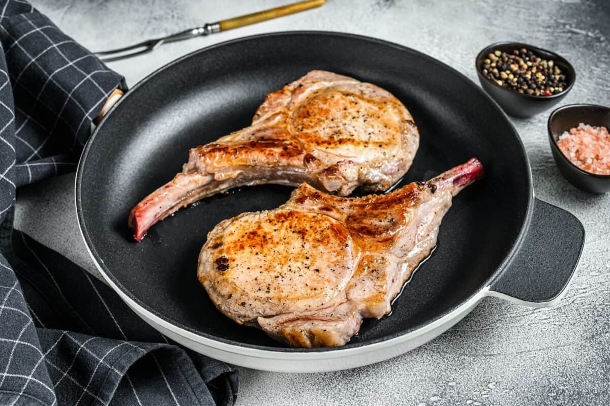 Roasted pork chop meat steak in a pan. White background. Top view