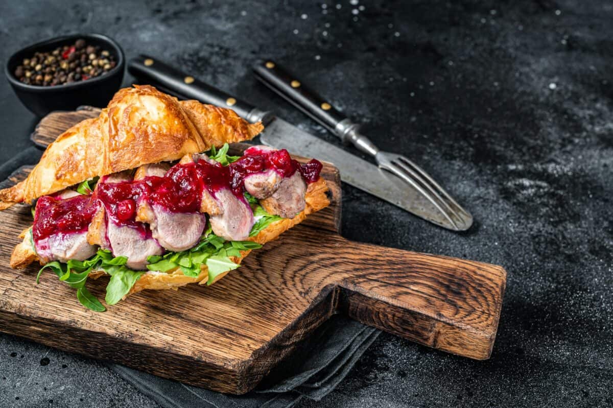Sandwich au croissant avec des tranches de steak de magret de canard, de la roquette et de la sauce.